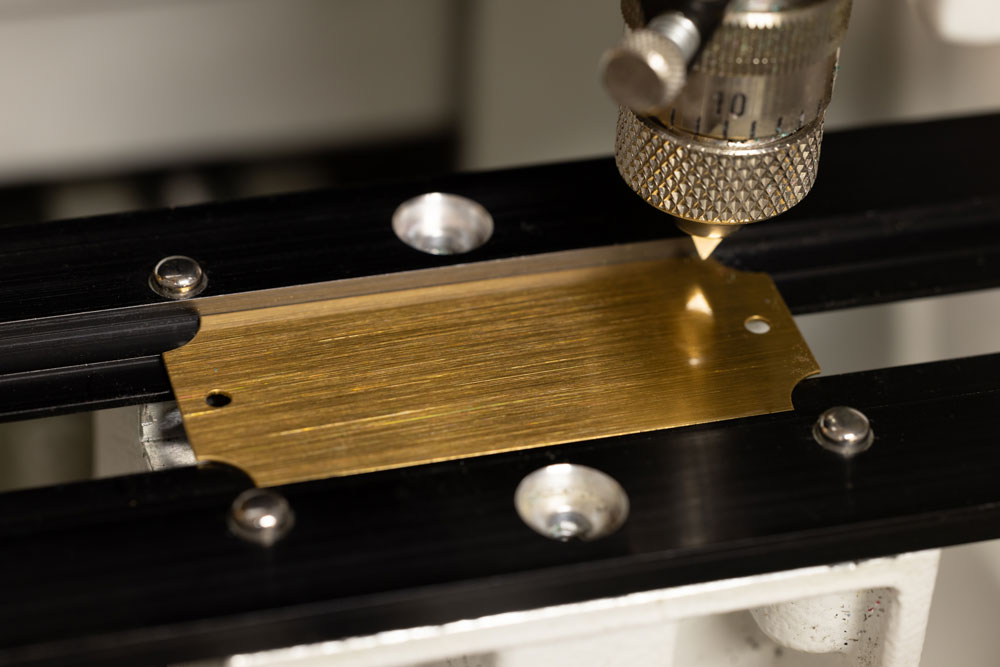 Gold metal piece being custom engraved with laser and rotary engraving